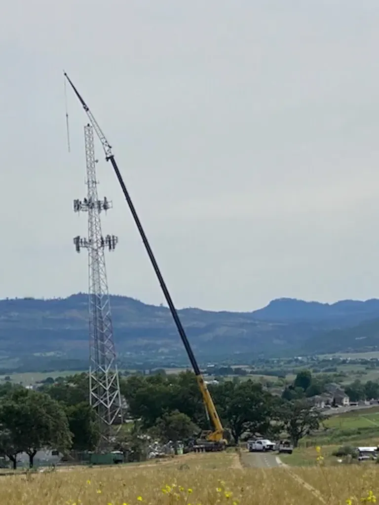 Long-boom crane by Jacked Co. reaching a high-altitude cellular tower for telecommunications infrastructure maintenance.