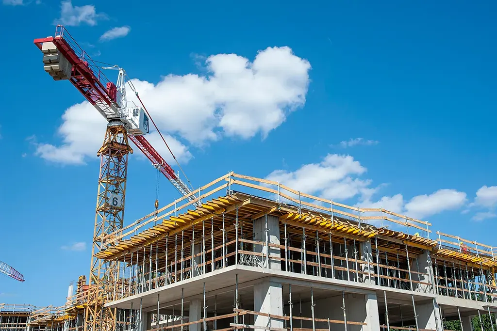 Tower crane at a commercial construction site during the structural framing phase under a clear blue sky.