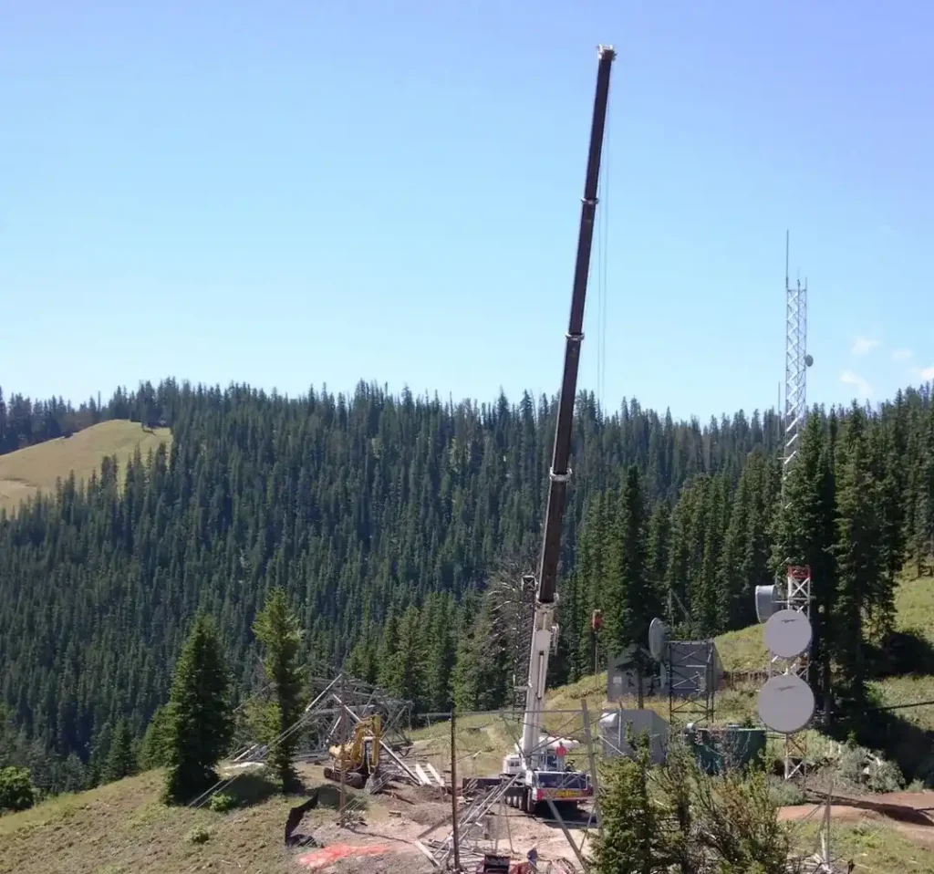High-reach crane at a remote mountain project site for telecommunications or utility tower installation.