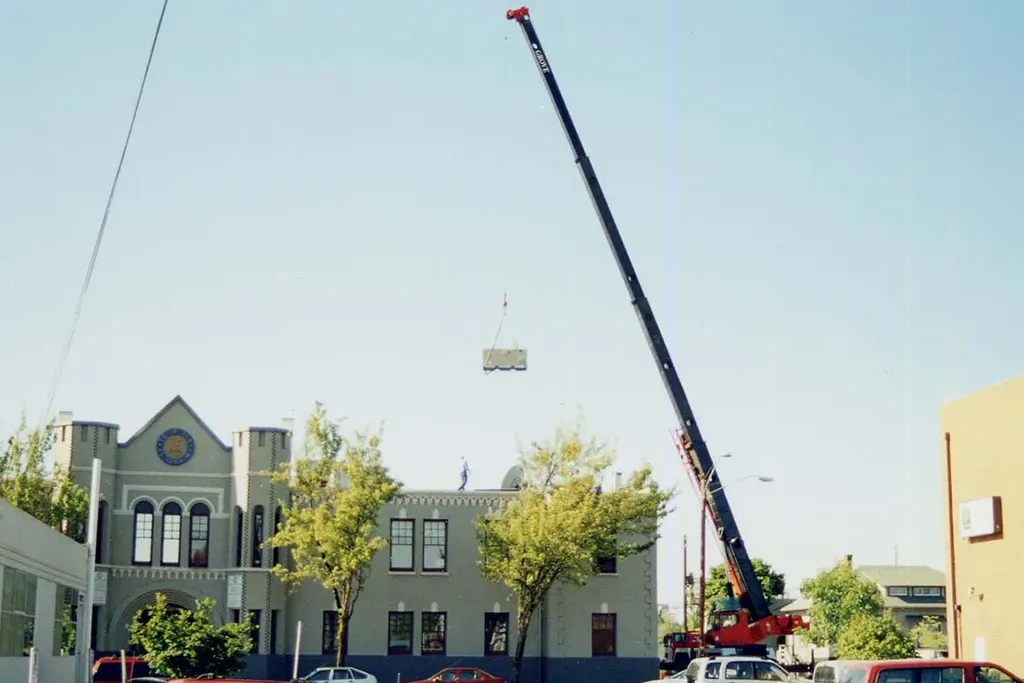 Jacked Co. hydraulic crane lifting a heavy HVAC unit onto the roof of a municipal commercial building.