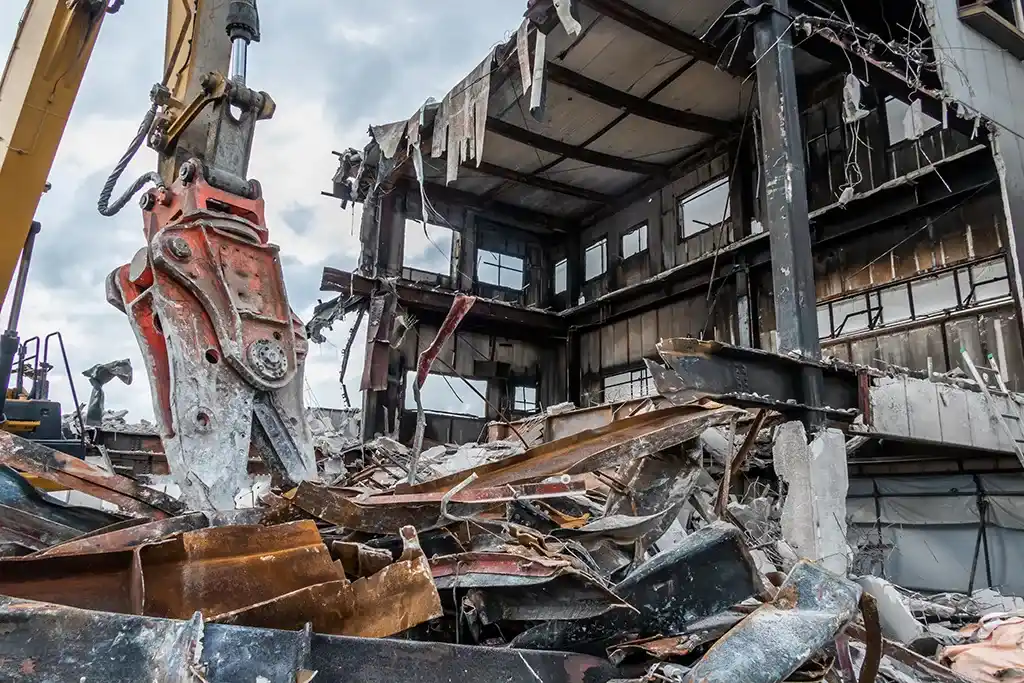 Heavy-duty hydraulic shear attachment on an excavator performing structural demolition of a steel-frame building.