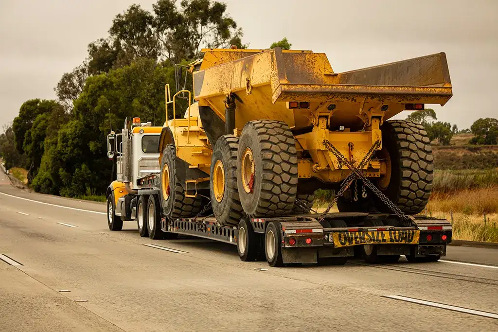 Oversize load transport of a large yellow articulated dump truck on a multi-axle heavy haul trailer.