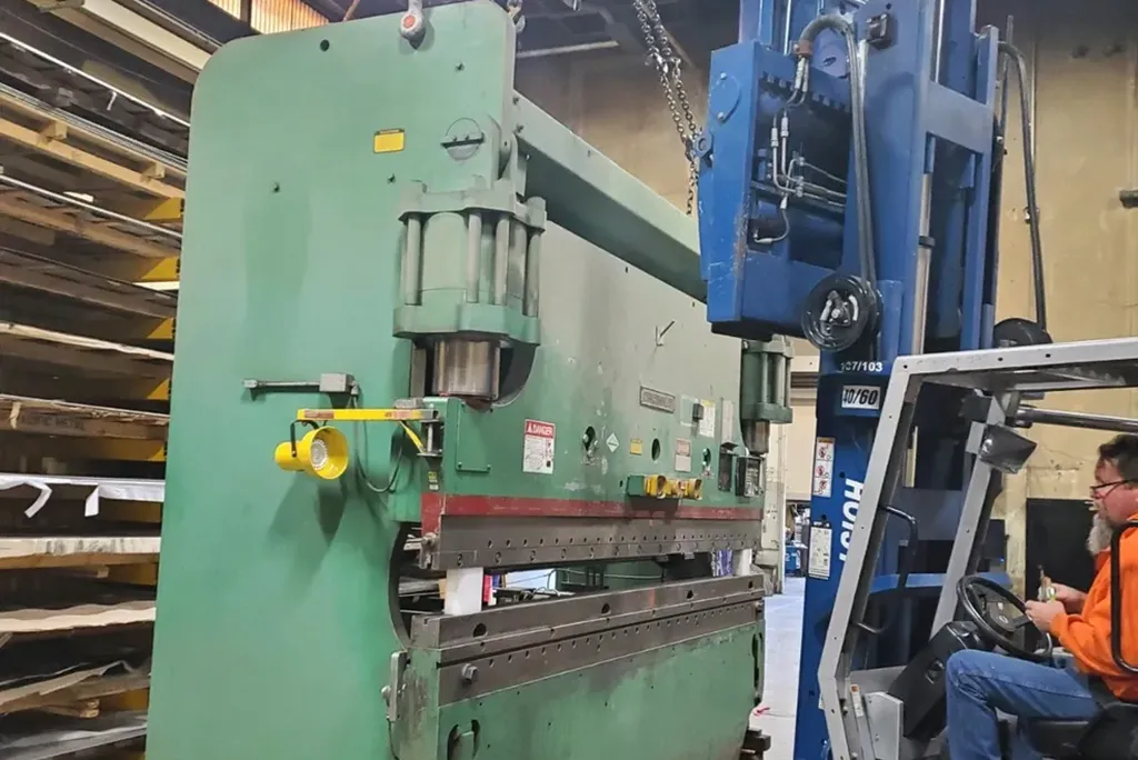 Precision machinery moving of a large green industrial metal press using a heavy-duty Hoist forklift.