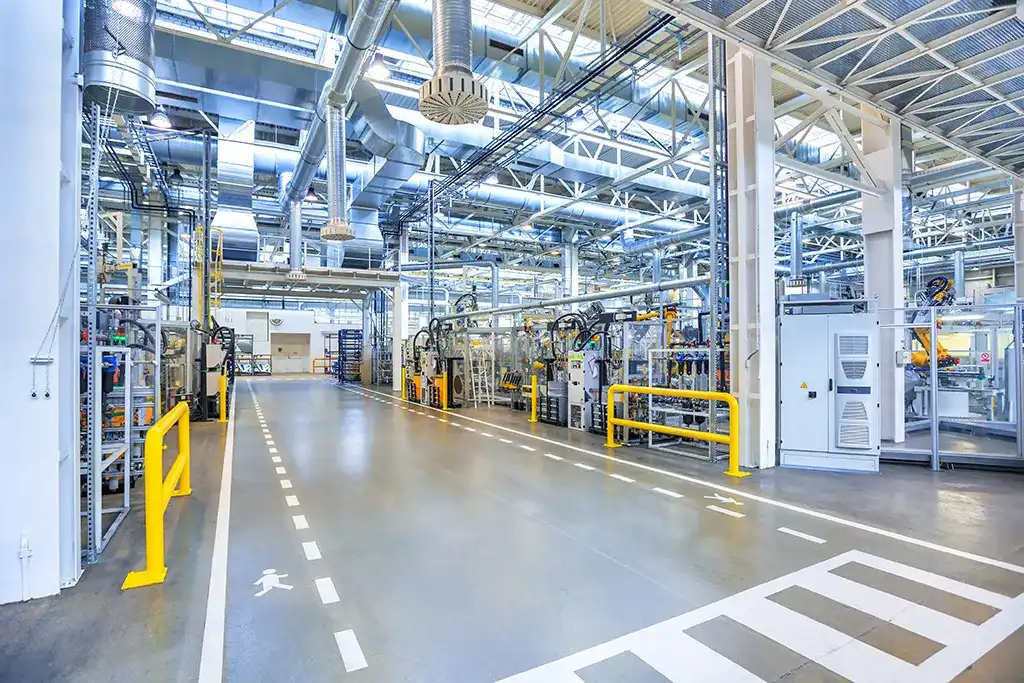 Clean, modern industrial manufacturing floor with robotic assembly lines and overhead ventilation systems.