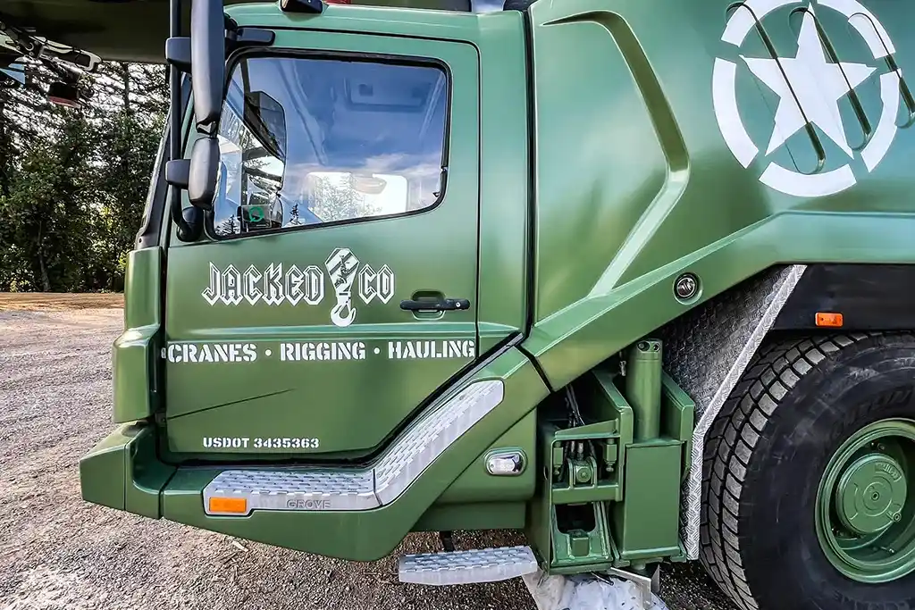 Side view of a Jacked Co. Grove crane truck in olive drab with custom military-style "Cranes Rigging Hauling" decals.