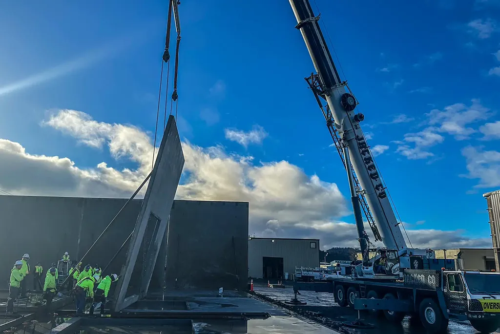 Jacked Co. mobile crane performing a tilt-up concrete wall panel installation with a specialized ground crew.