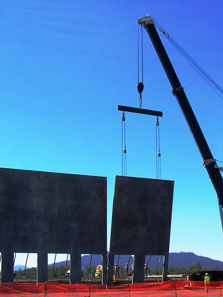 Precision tilt-up concrete wall installation using a Jacked Co. crane and spreader bar at a new construction site.