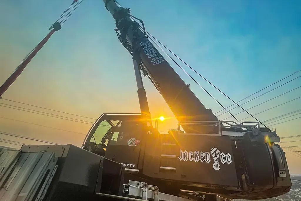 Silhouette of a Jacked Co. branded crane cabin against a sunset, highlighting the company logo and boom.