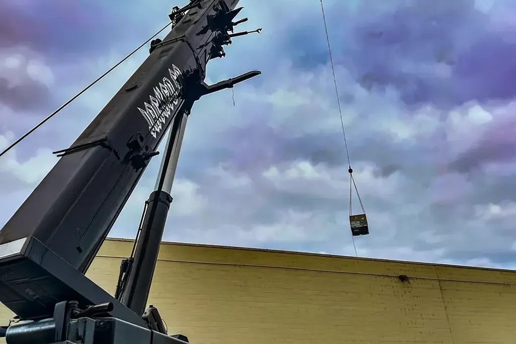 Close-up of a Jacked Co. crane boom lifting a mechanical unit onto the roof of a large industrial building.