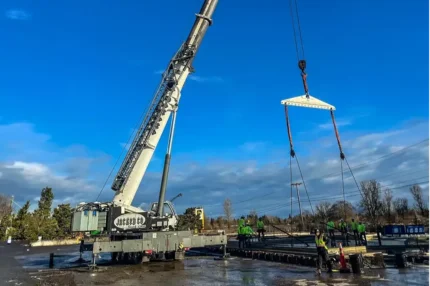 Jacked Co. mobile crane using a spreader bar for a precision lift on a wet construction site.