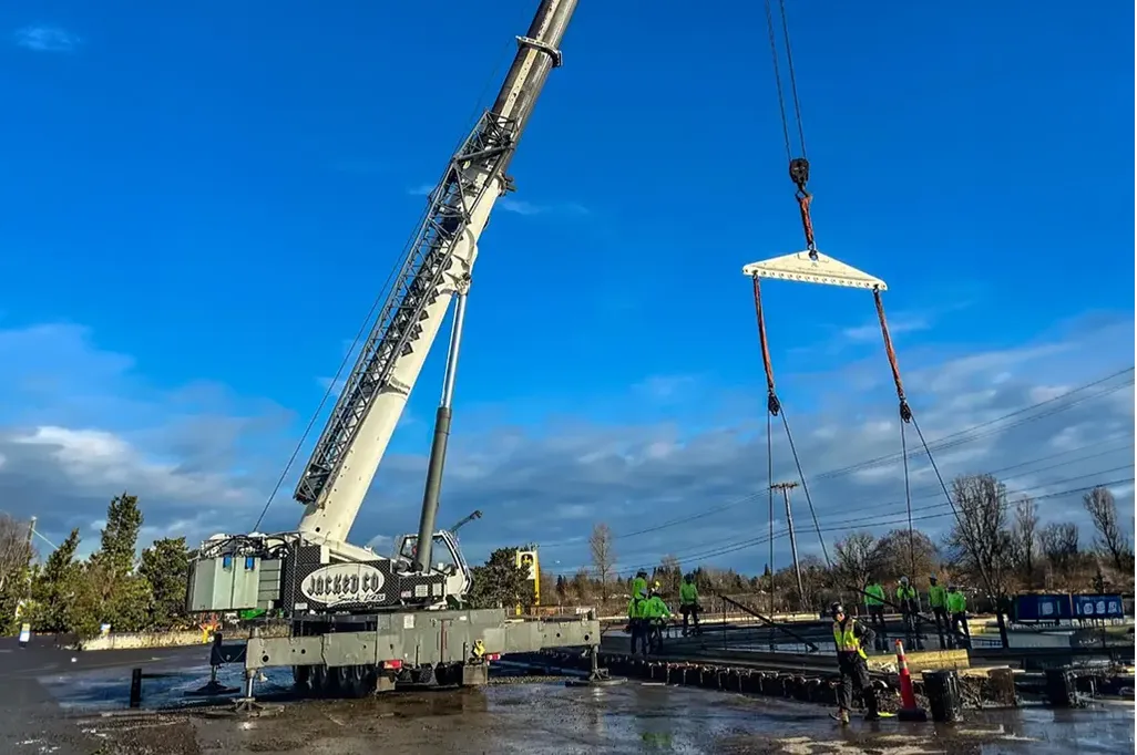 Jacked Co. mobile crane using a spreader bar for a precision lift on a wet construction site.