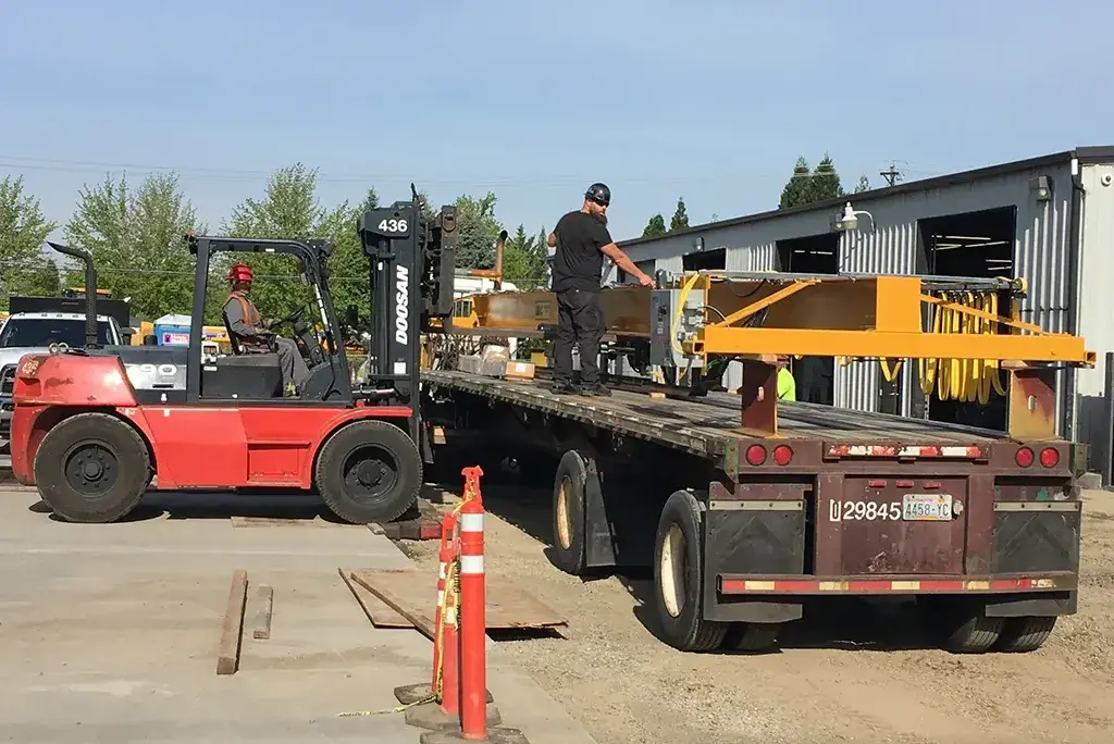 Precision equipment loading with a Doosan forklift onto a flatbed trailer for a Jacked Co. hauling project.