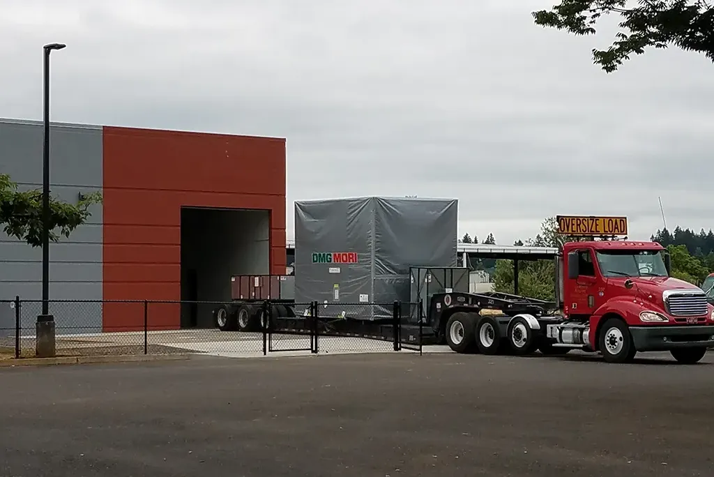 Red Jacked Co. semi-truck transporting a large, tarped DMG MORI CNC machine with "Oversize Load" signage.