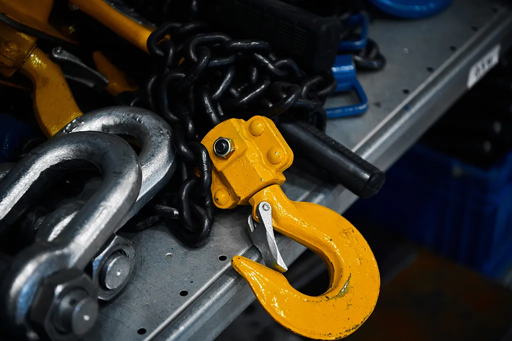Close-up of heavy-duty rigging hardware including a yellow swivel hoist hook, steel chains, and shackles.