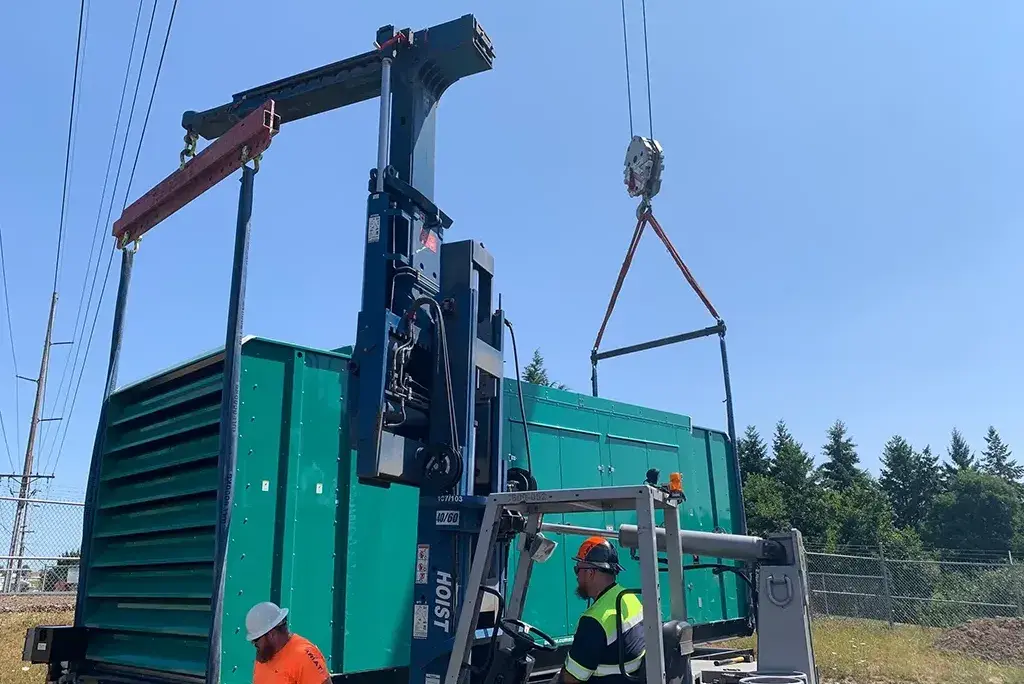Jacked Co. rigging crew using a heavy-duty Hoist forklift and crane to position a green industrial generator.