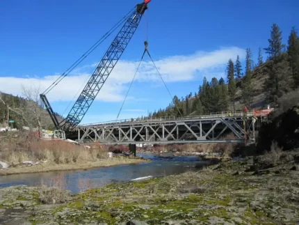 Lattice boom crane by Jacked Co. positioning a large steel truss bridge over a river for a civil infrastructure project.