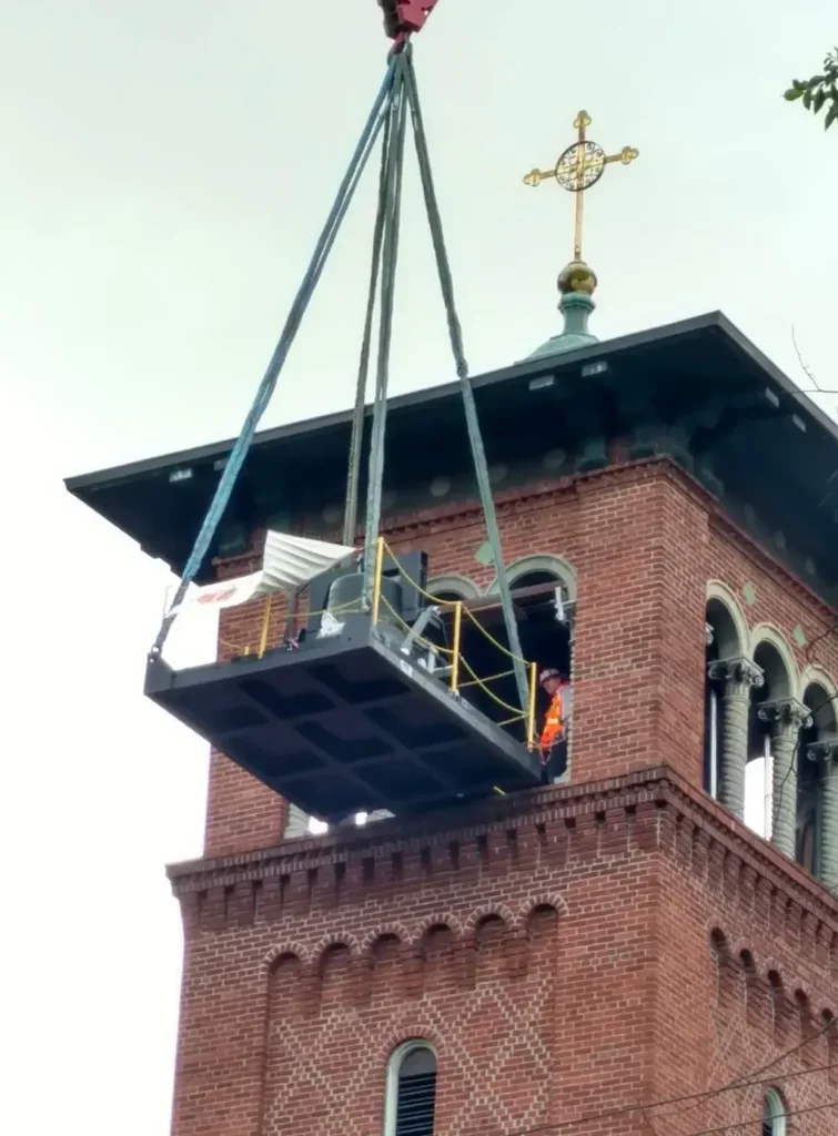 Precision rigging by Jacked Co. lifting a historic bell assembly out of a brick cathedral bell tower.