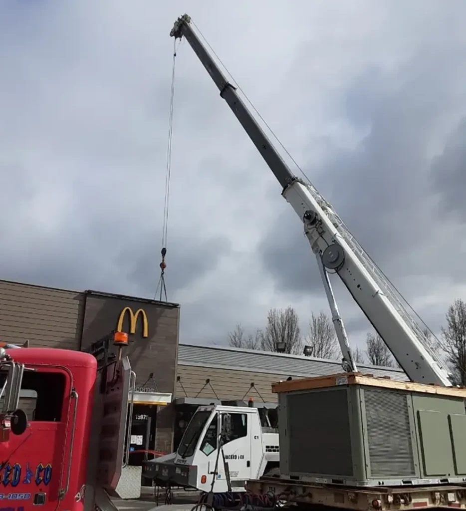 Jacked Co. crane truck hoisting a heavy industrial HVAC unit onto the roof of a commercial restaurant building.