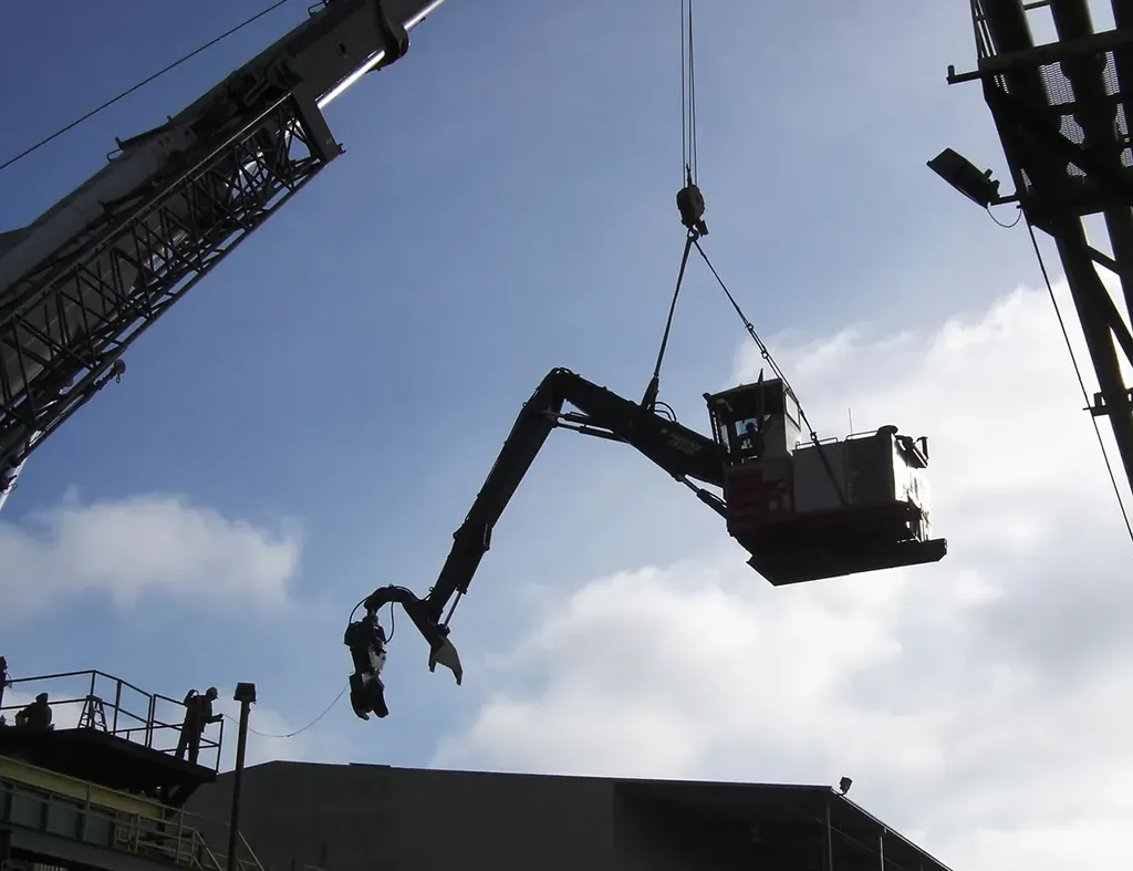 Silhouette of a mobile crane from Jacked Co. lifting heavy construction machinery at an industrial job site.
