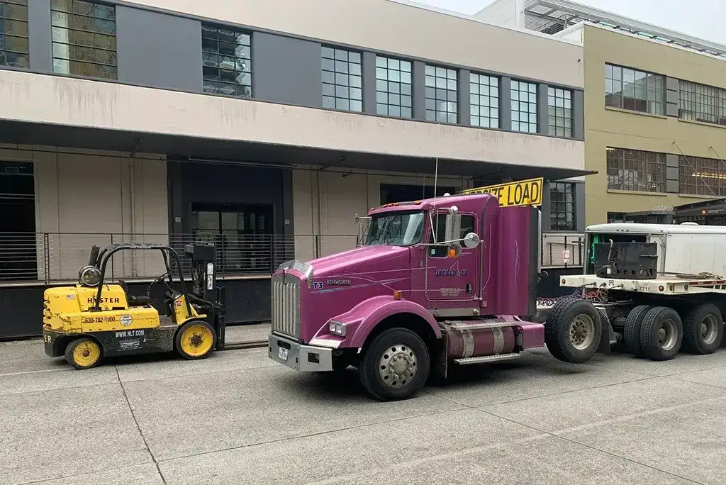 Purple Jacked Co. Kenworth heavy-haul truck staged with a Hyster forklift for machinery transport.