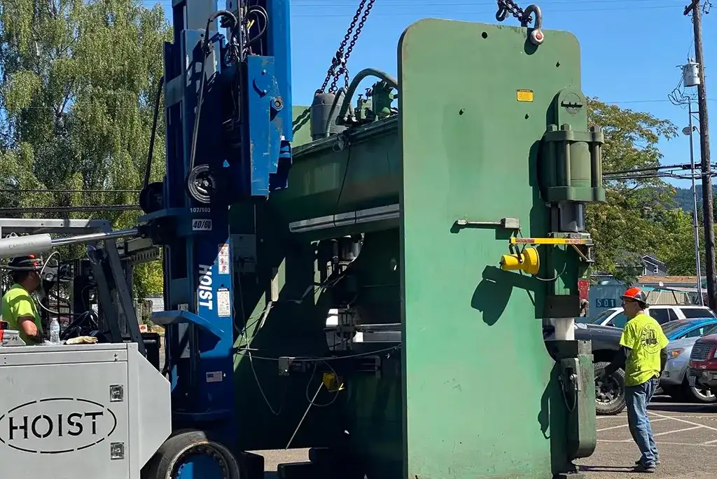 Heavy-duty Hoist forklift by Jacked Co. performing a precision move of a large green industrial metal press.