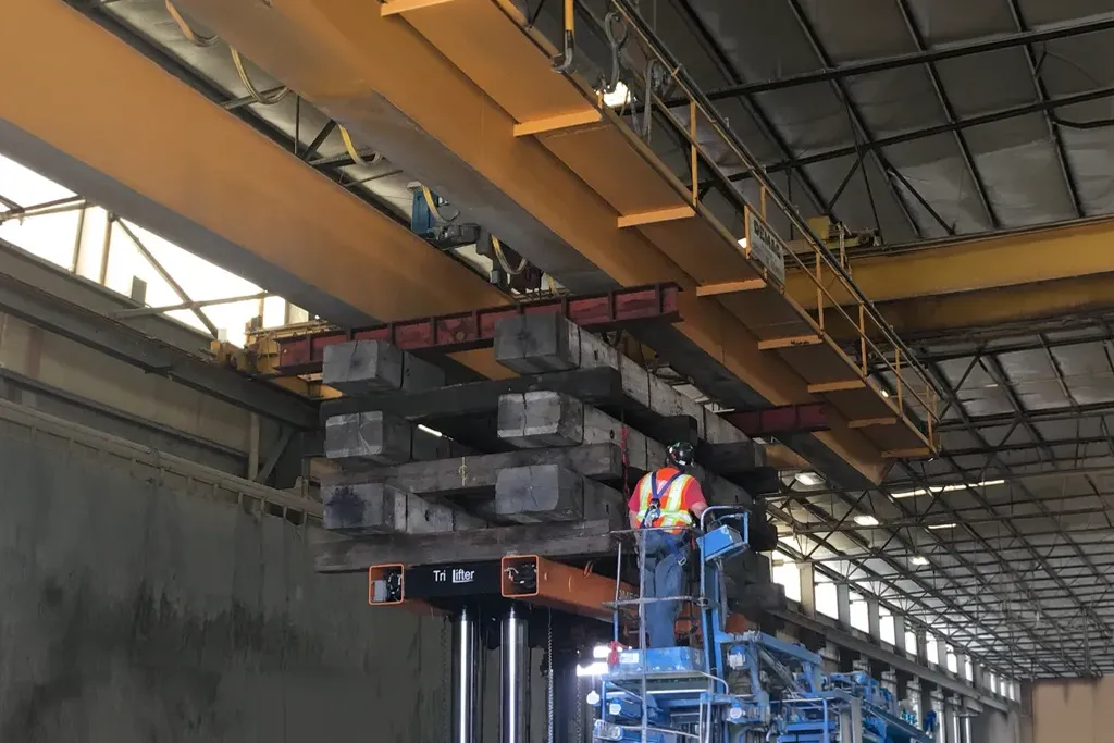Specialized Tri-lifter and overhead rigging team moving heavy timber supports inside an industrial warehouse.