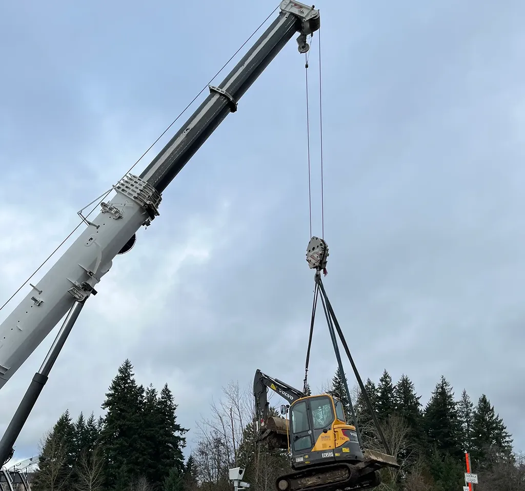 Jacked Co. mobile crane performing a specialized lift of a Volvo mini excavator at a construction site.