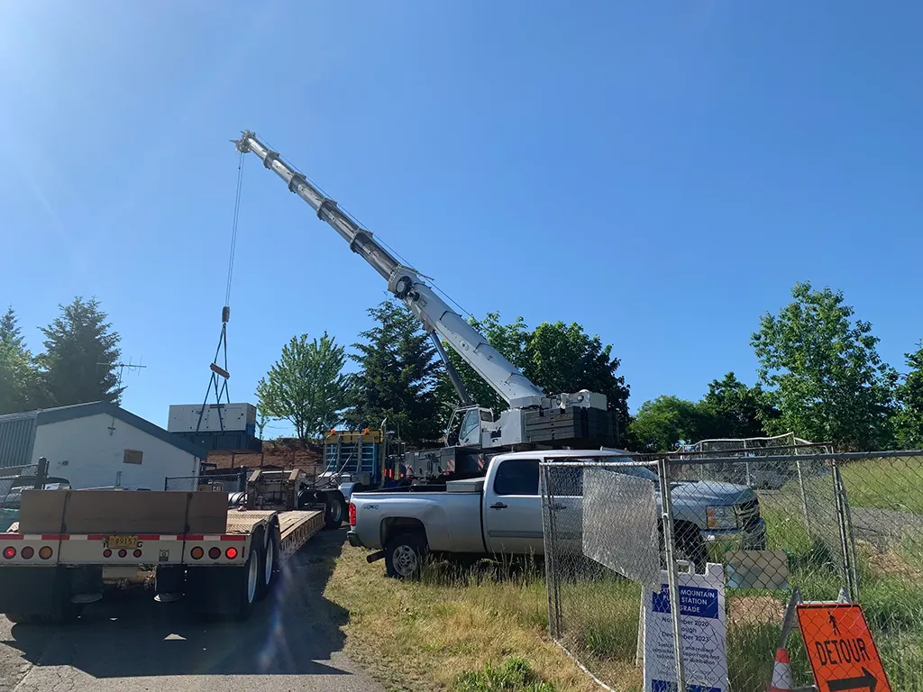 Jacked Co. crane staged with a heavy-haul flatbed trailer for a machinery transport project at a utility substation.