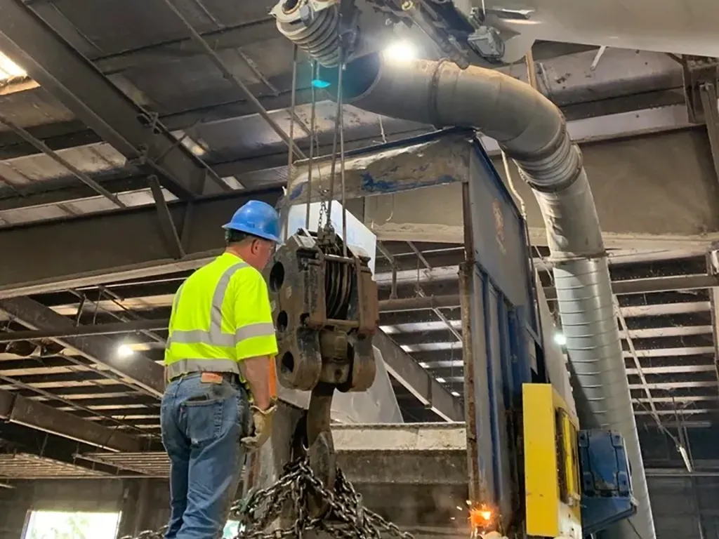 Precision industrial rigging services inside a manufacturing plant, showing a worker monitoring a heavy hoist lift.