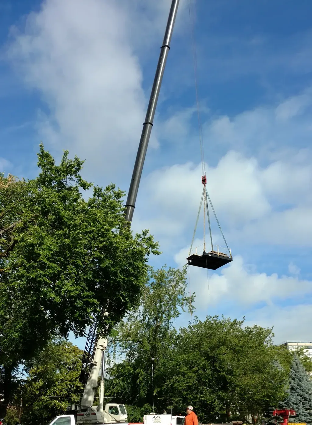 High-reach mobile crane by Jacked Co. hoisting a heavy material platform above a treeline for a commercial project.