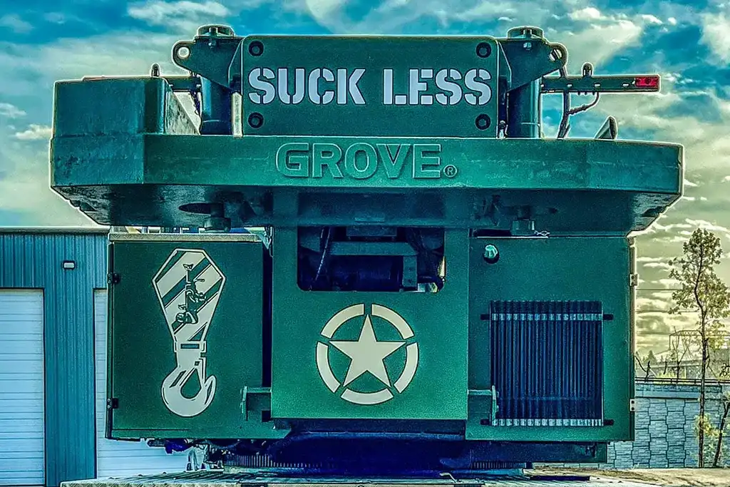Rear view of a Jacked Co. Grove crane featuring a custom "Suck Less" olive drab paint scheme and military-style branding.