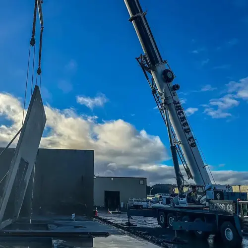 Jacked Co. mobile crane installing a tilt-up concrete wall panel with a specialized ground crew.