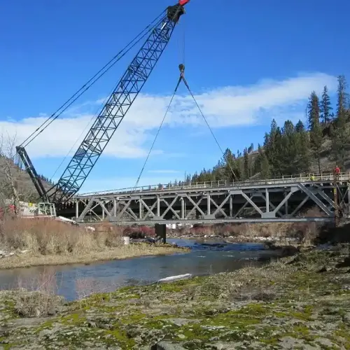 A Jacked Co. lattice boom crane positioning a large steel truss bridge over a river for a civil infrastructure project.