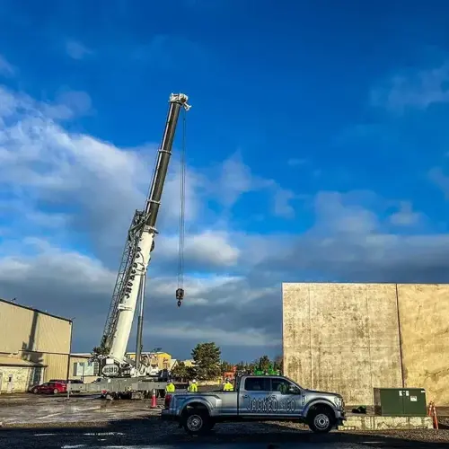 A Jacked Co. mobile crane with its boom extended high into the air, parked behind a silver company pickup truck at an industrial construction site